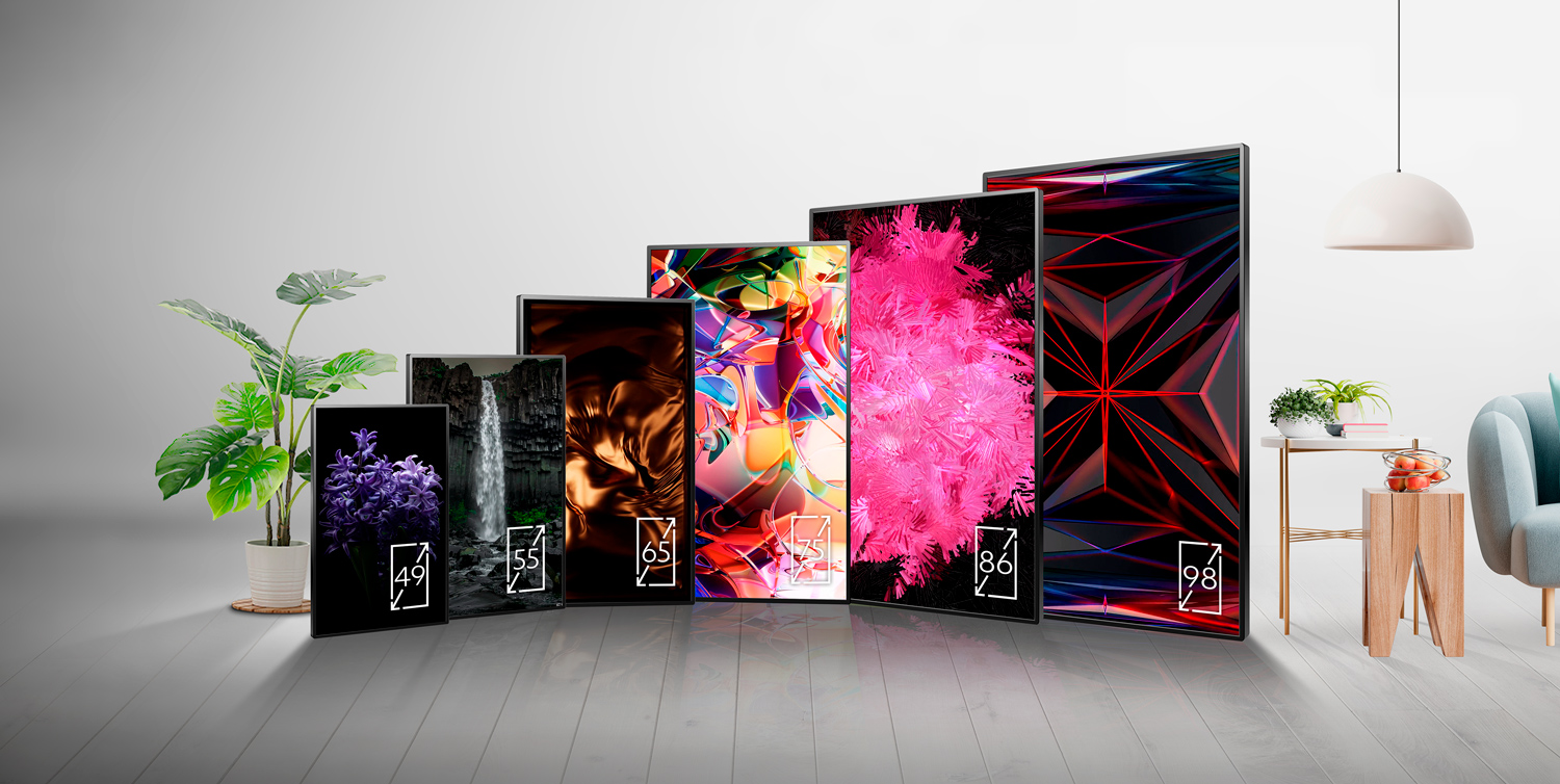 A row of six flat-screen TVs in various sizes, each displaying vibrant abstract and nature-themed images, stands in a modern, minimal living room with plants, a lamp, and a chair in the background.