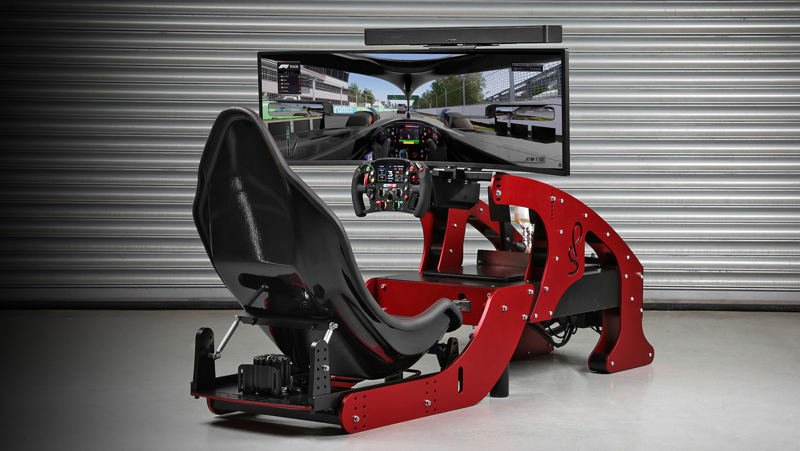 A red Driving Simulators cockpit setup with a racing seat, steering wheel, pedals, and a large screen displaying a racing game, all positioned in front of a metal roller door.